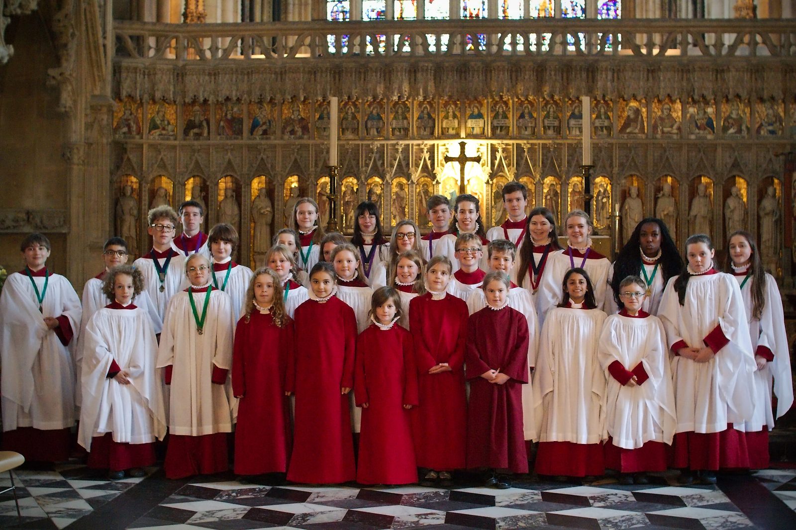 Young choristers of the Minster Choir, in red cassocks and white surplices, before the gilded screen.